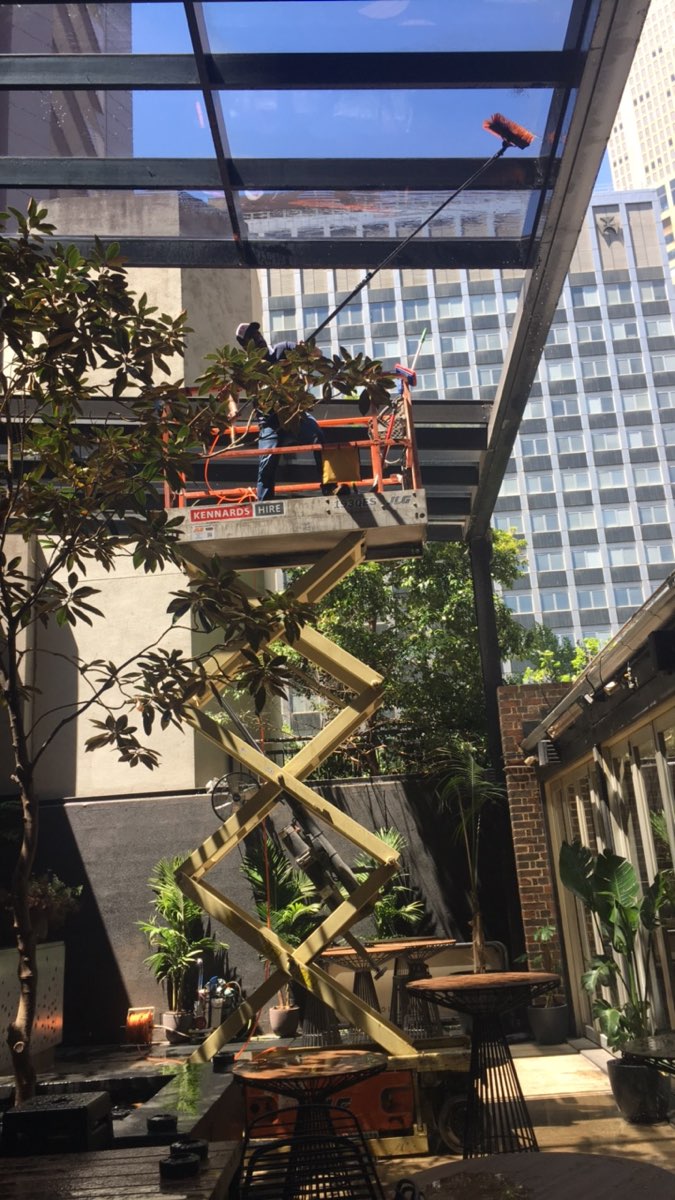 Professional cleaner on a scissor lift washing a glass canopy with a water-fed pole