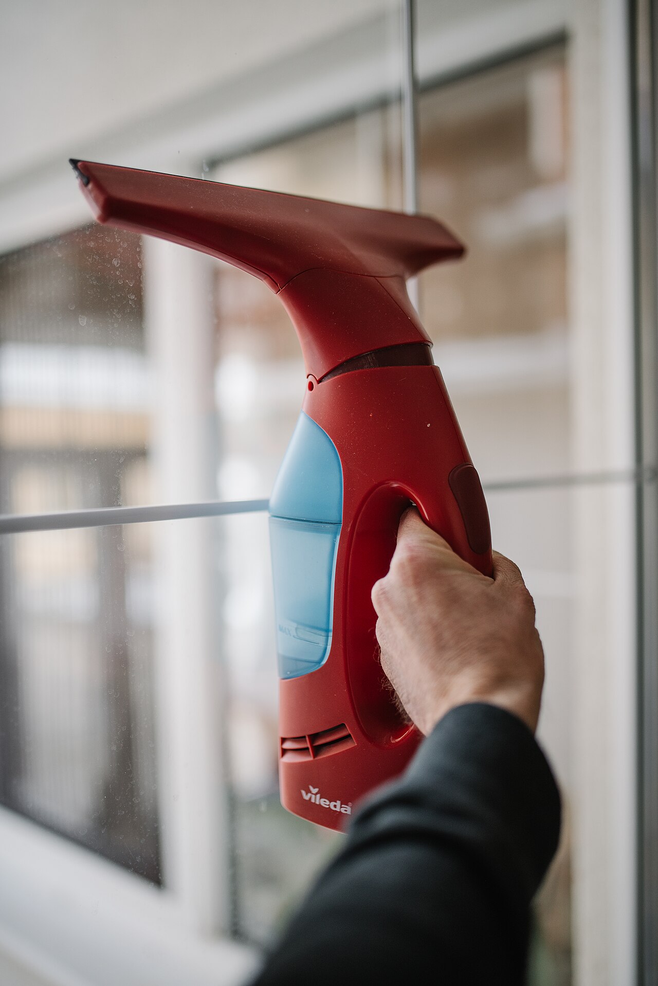 Hand holding a window vacuum squeegee tool against a home window