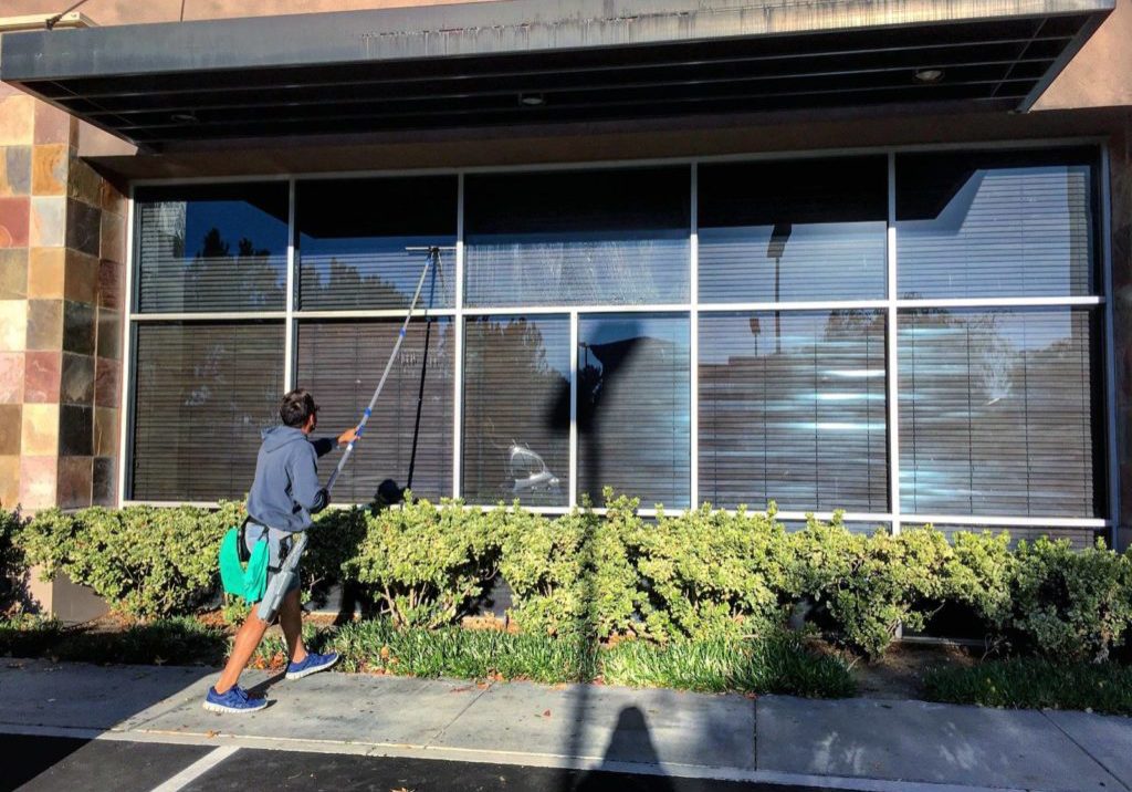 Window cleaner using a water-fed extension pole to clean large commercial shopfront windows