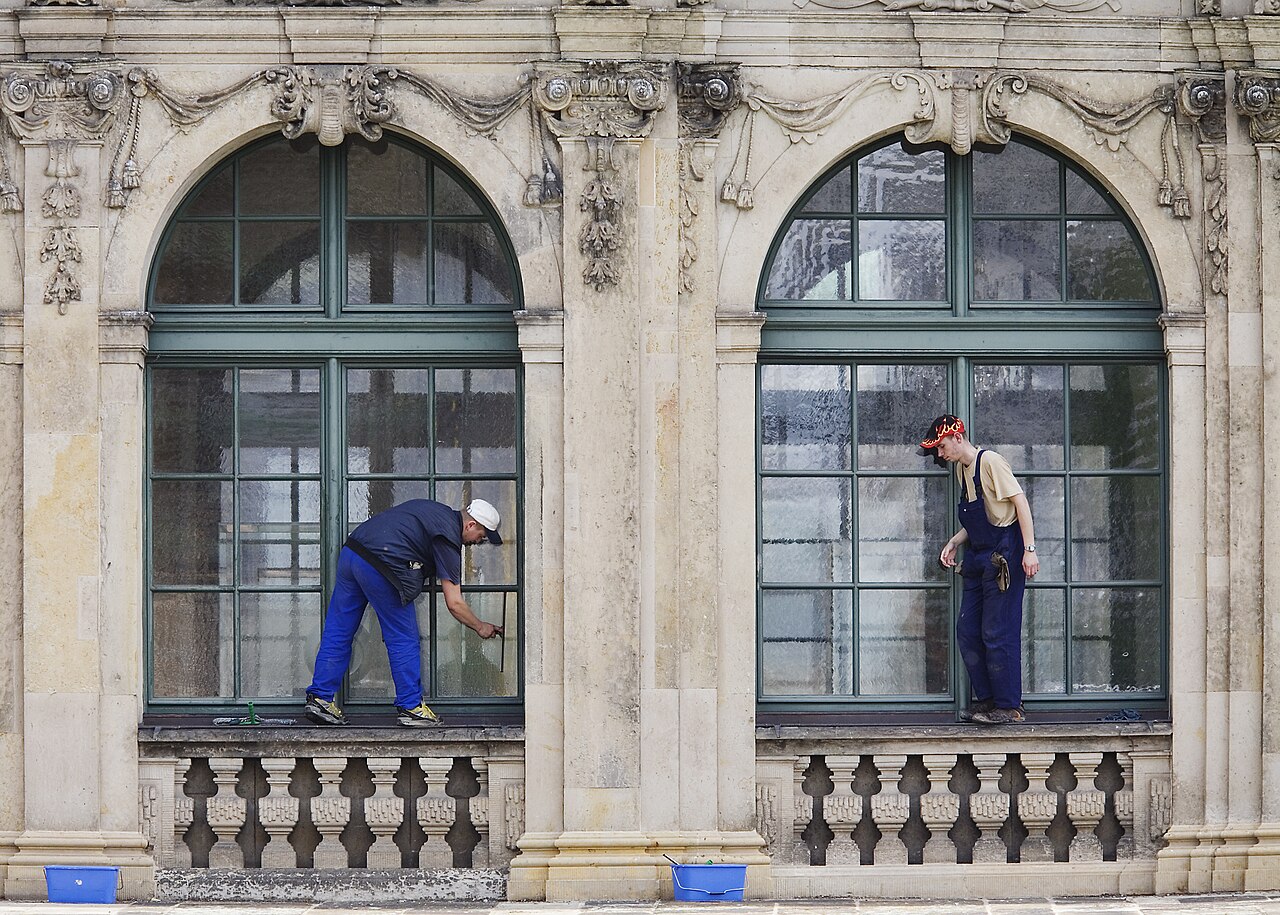 Two professional window cleaners hand-cleaning large multi-pane windows with squeegees and buckets